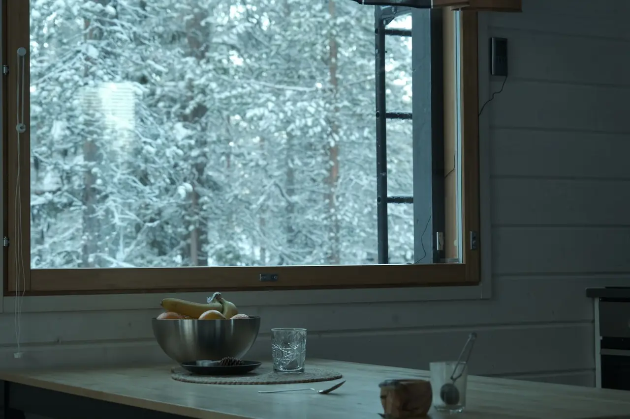 Valoisa skandinaavinen keittiö ja ruokailutila, josta avautuu suuri panoraamaikkuna lumiseen metsämaisemaan