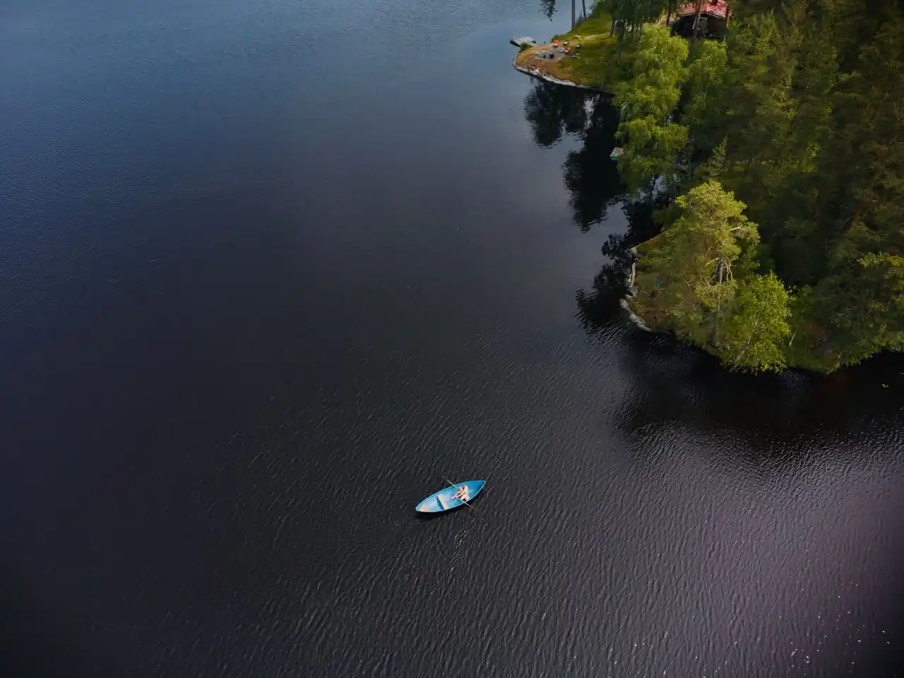 Kirkas kesäinen järvimaisema tyvenellä vedellä ja vehreällä metsällä